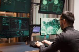 Cybersecurity professional analyzing data on multiple monitors in a secure operations center.
